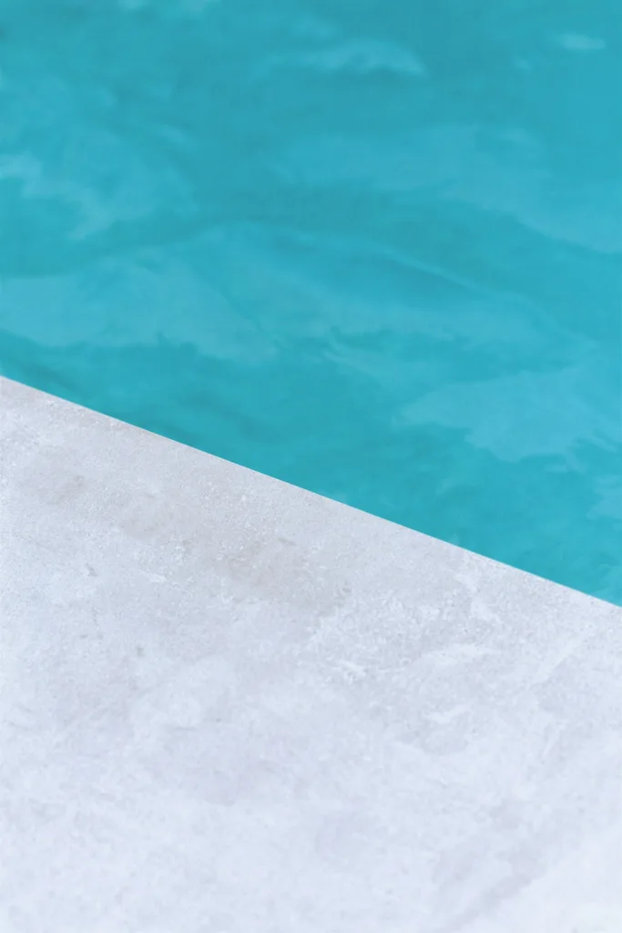 Diagonal view of turquoise pool water beside a pale concrete edge