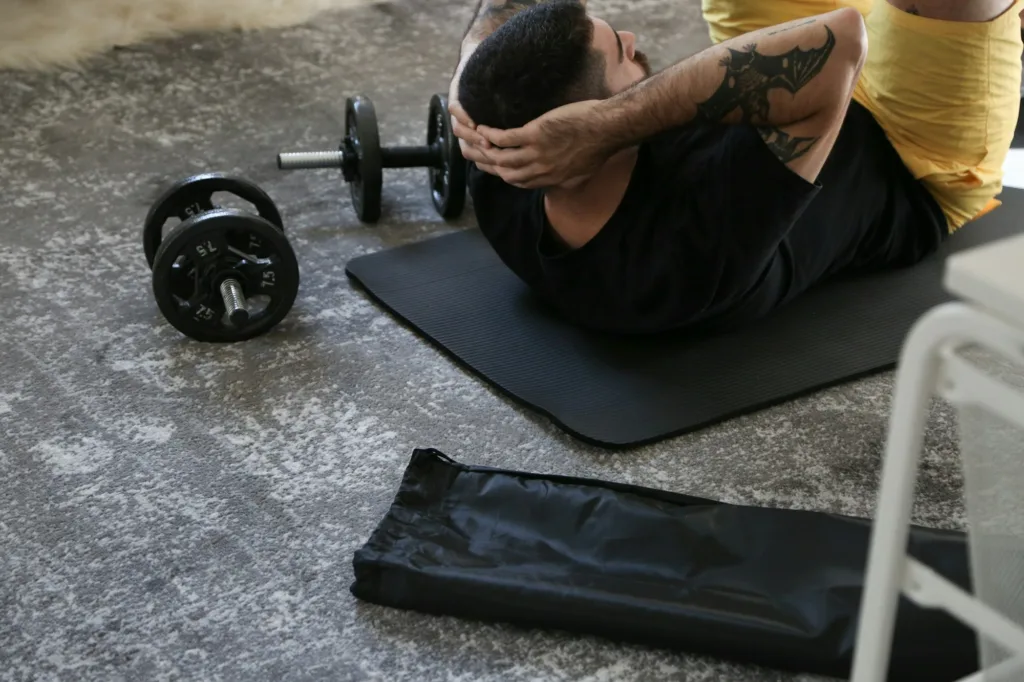 Man doing sit-ups on a mat with dumbbells nearby in a gym or home workout space