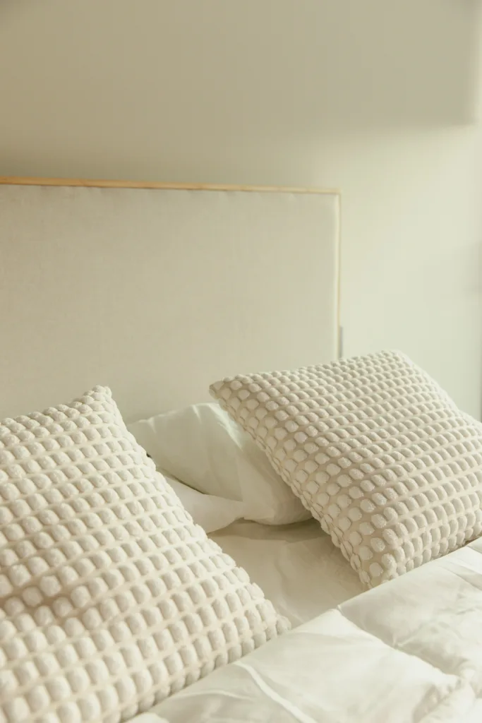 Neutral bedroom with a beige headboard and two textured cream pillows on a white bed